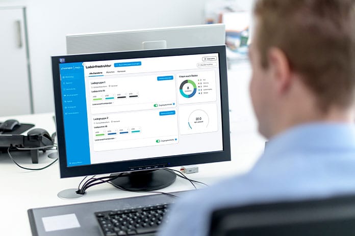 Eine Person sitzt an einem Büroarbeitsplatz vor einem Computerbildschirm. Auf dem Monitor ist das Sonepar Betreiber Dashboard zu sehen. Die Oberfläche zeigt mehrere Auswertungs- und Statusanzeigen, darunter Balken, farbige Markierungen und kreisförmige Diagramme. Links befindet sich ein blaues Navigationsmenü. Die Person ist nur von hinten und unscharf zu erkennen. Die Szene vermittelt das Arbeiten mit einer digitalen Verwaltungs- und Analyseanwendung in einem Büro.