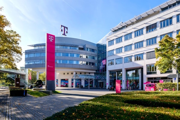 Exterior view of a modern office building with pink T-Mobile branding and a large T logo against a blue sky, toward a glass entrance.