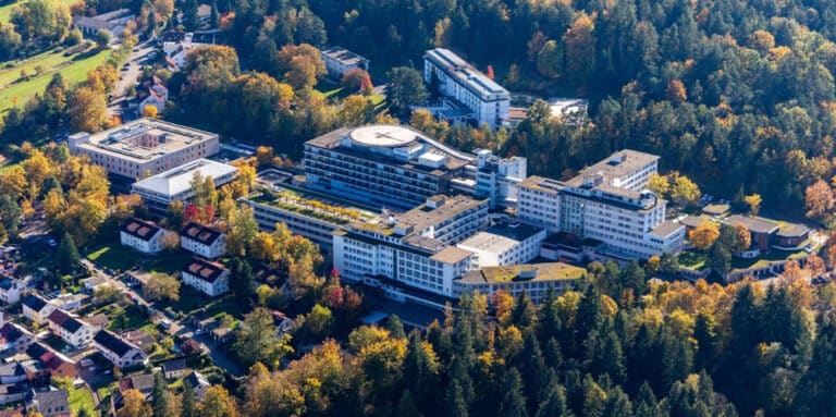 Aerial view of a hospital campus with white buildings surrounded by autumn trees in fall colors.