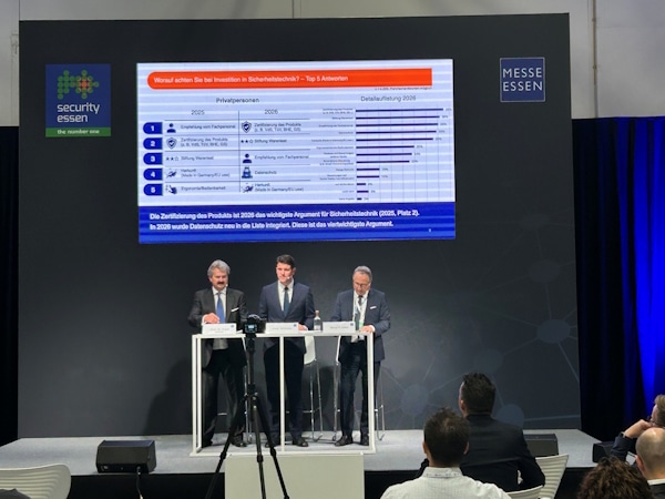 Three men in suits stand behind podiums on a stage at a conference, with a large screen displaying a bar-chart infographic behind them, and logos for Messe Essen and security Essen visible on stage.